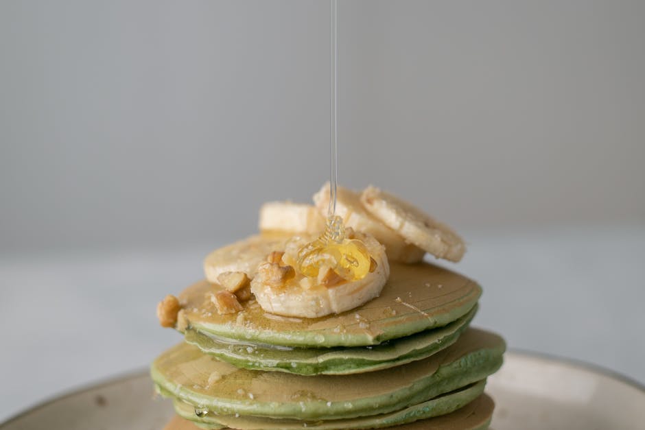 Appetizing sweet pancakes with honey and pieces of fresh banana on gray background